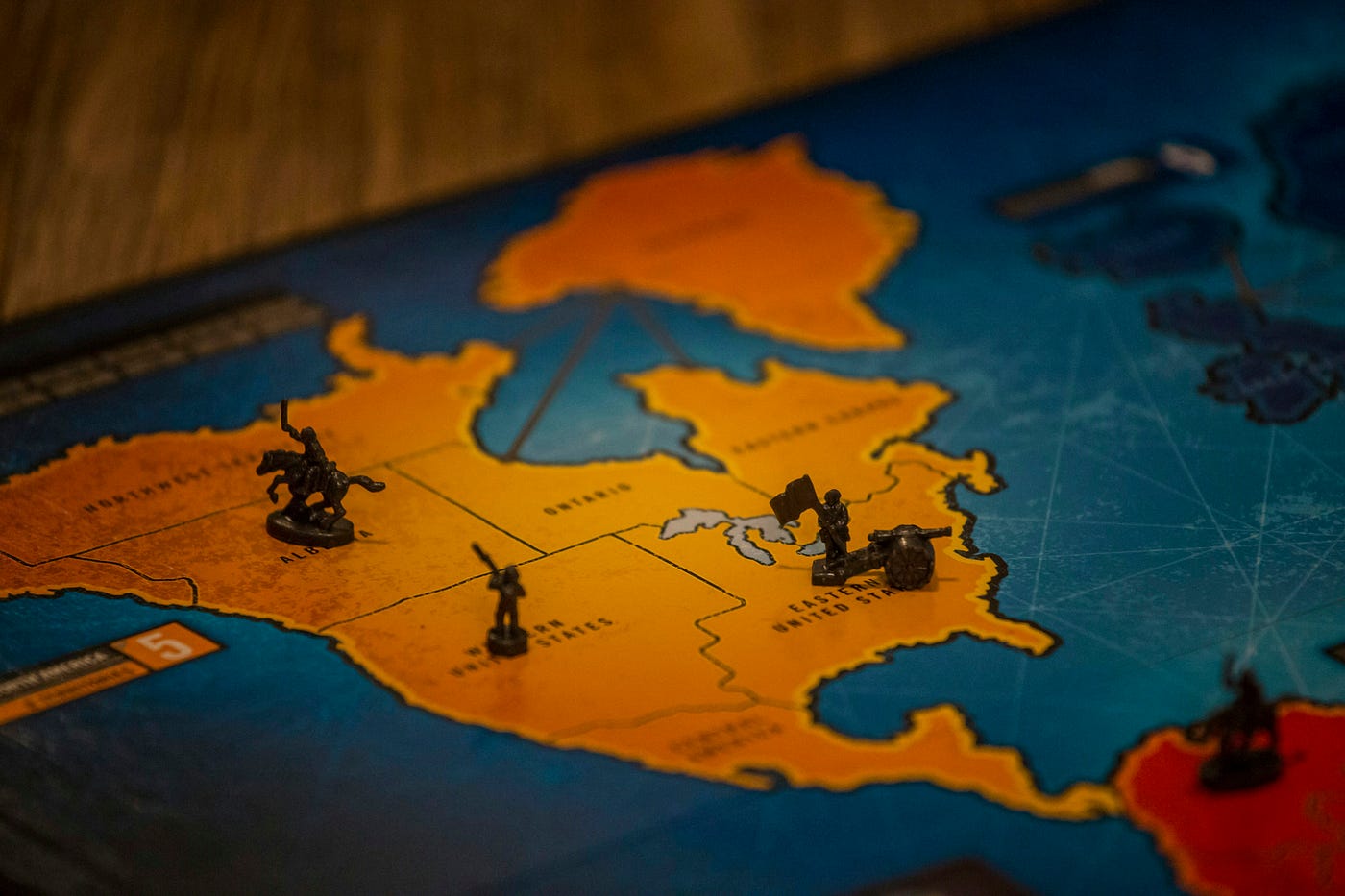 A close, shallow-focus shot of a Risk board: dark plastic pieces holding territory across an orange North America.