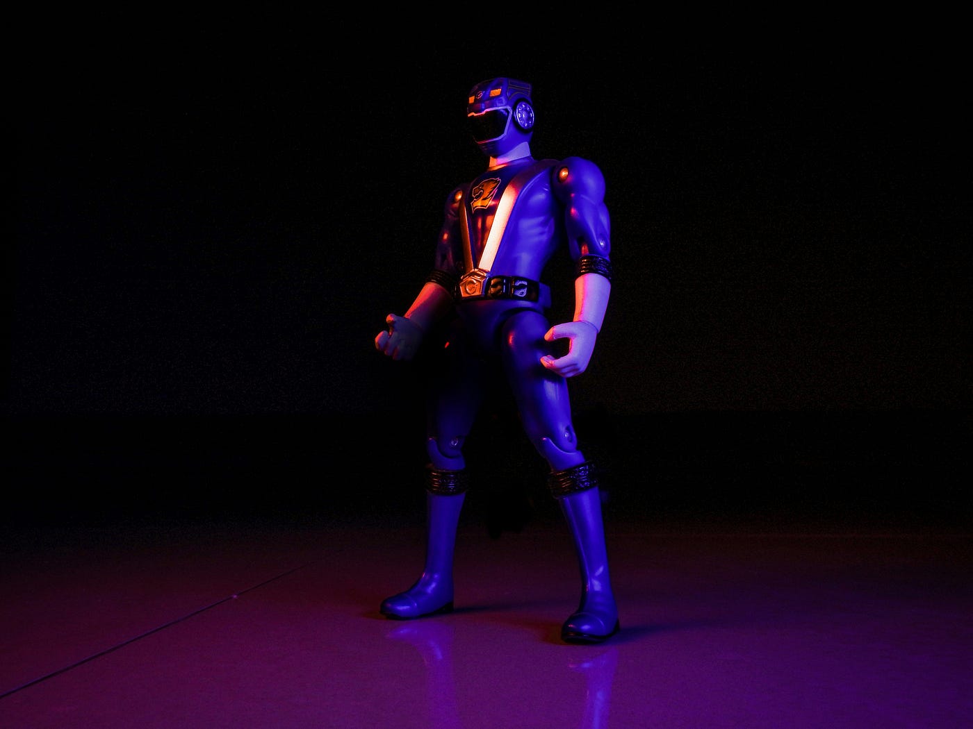 A costumed superhero action figure posed alone under purple and orange light against a black background.