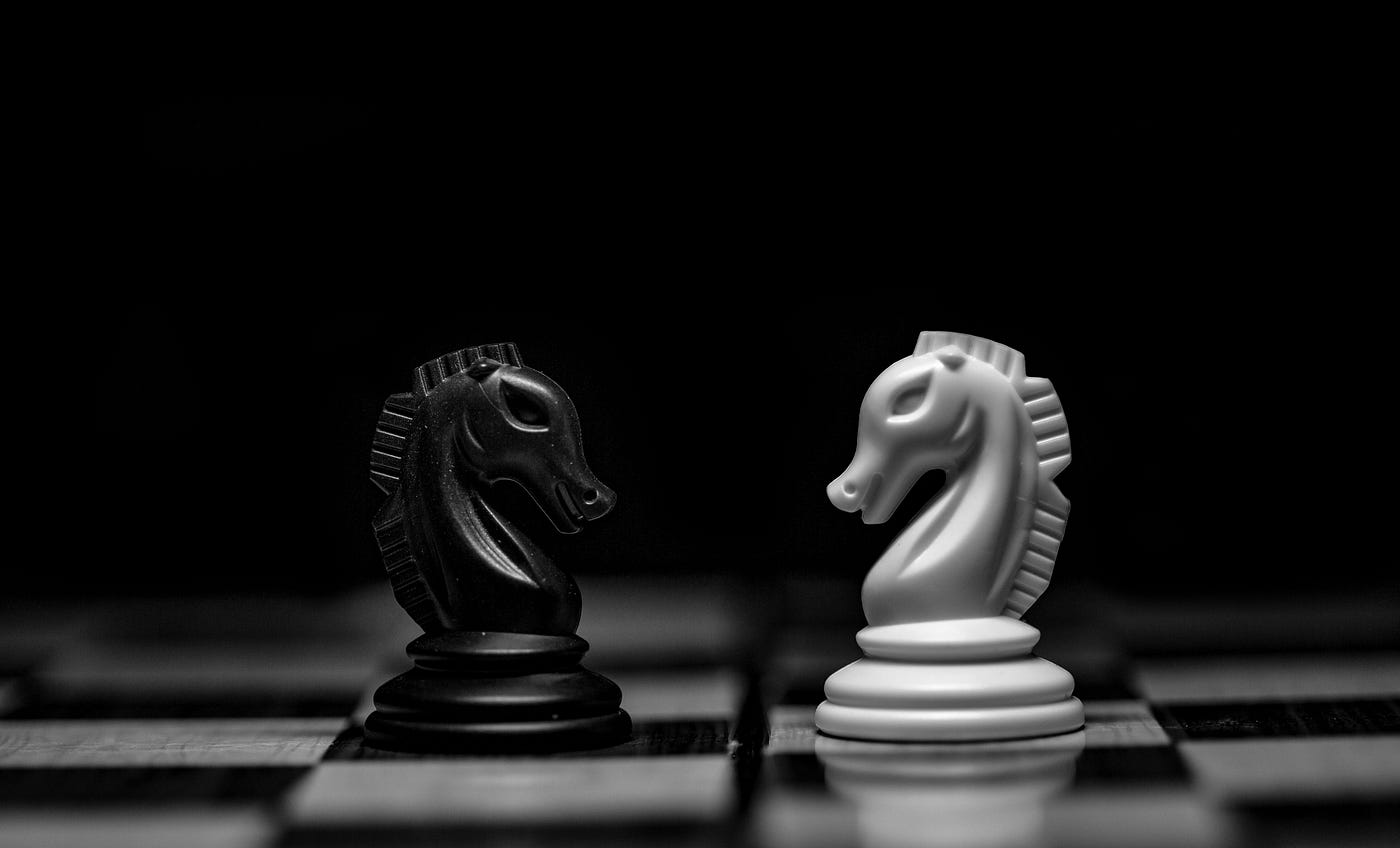 A black knight and a white knight facing each other across a chessboard in stark black-and-white light.