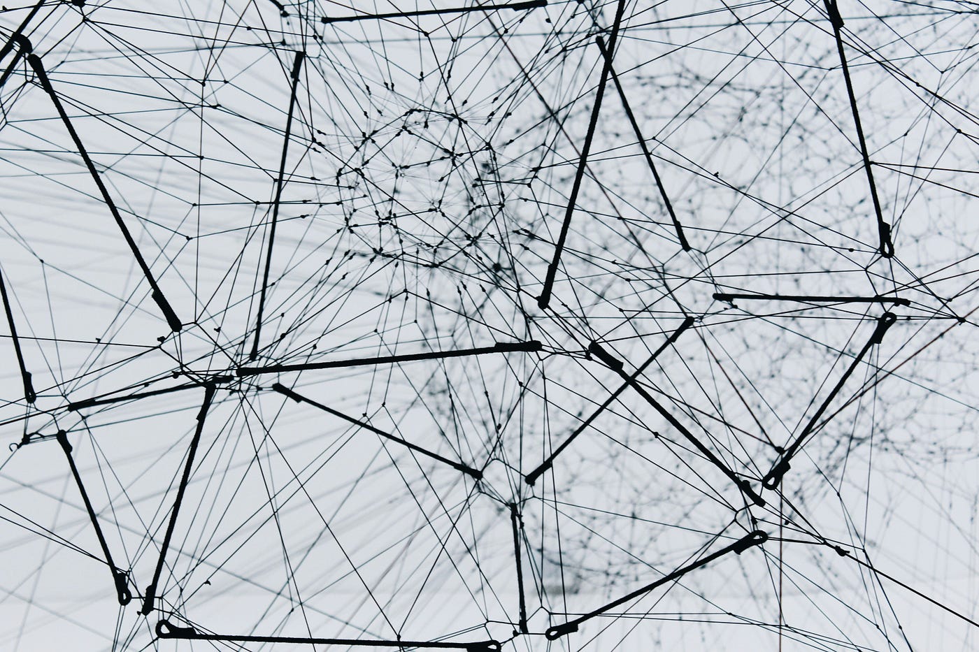 A dense black web of taut threads and struts against a pale sky, forming an irregular lattice of connected nodes.