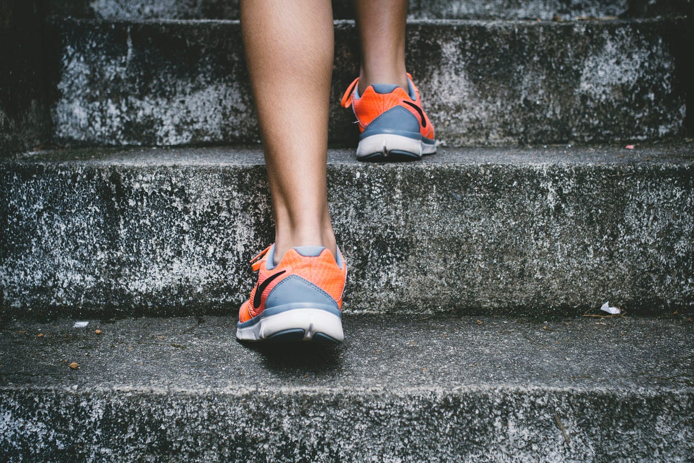 Close view from behind of a runner's legs in orange trainers climbing a flight of weathered concrete steps.