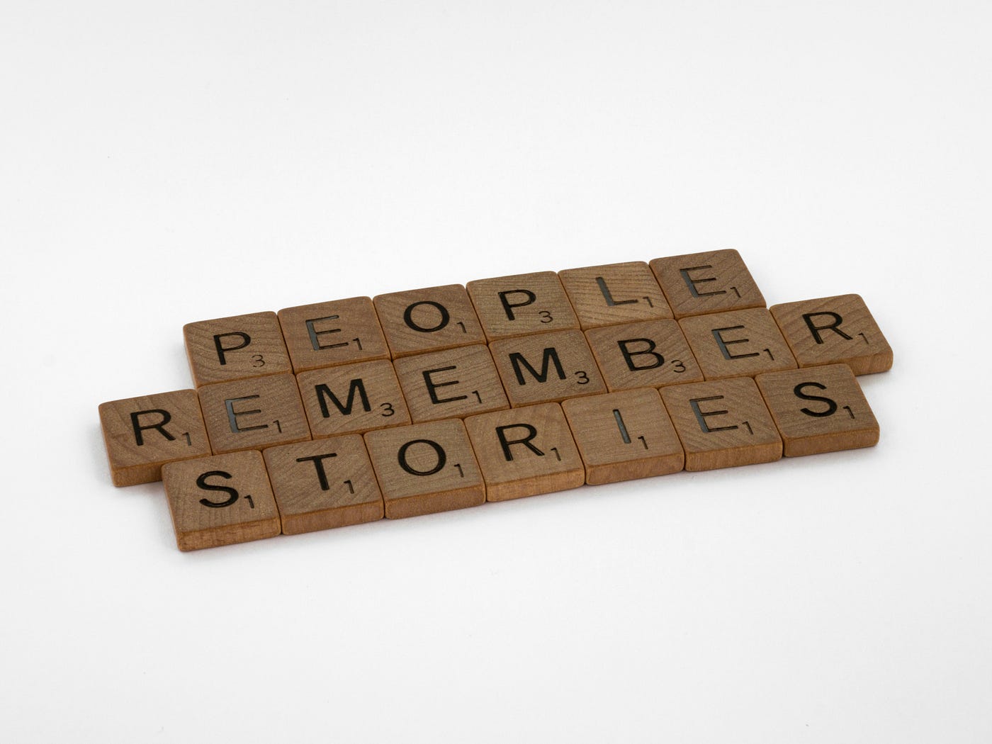 Wooden Scrabble tiles laid out on a white surface spelling 'PEOPLE REMEMBER STORIES'.
