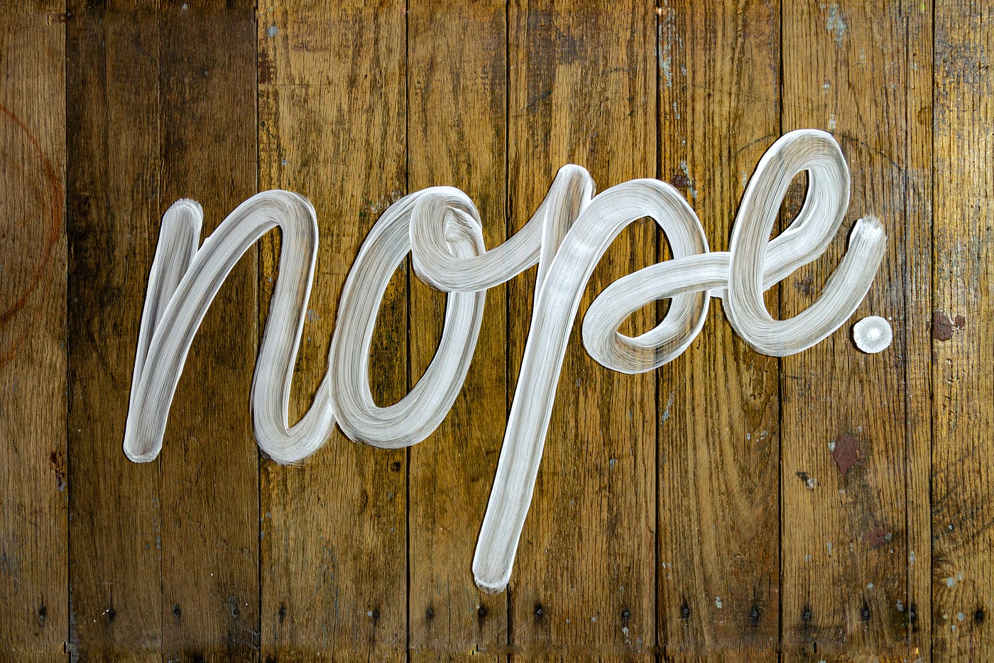 The word 'nope.' painted in large white brushstroke script across a scuffed wooden floor.