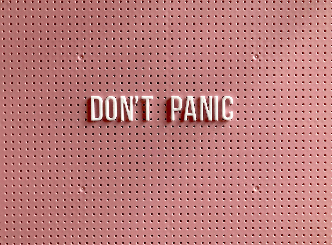White plastic letters spelling 'DON'T PANIC' pressed into a dusty-pink perforated pegboard.