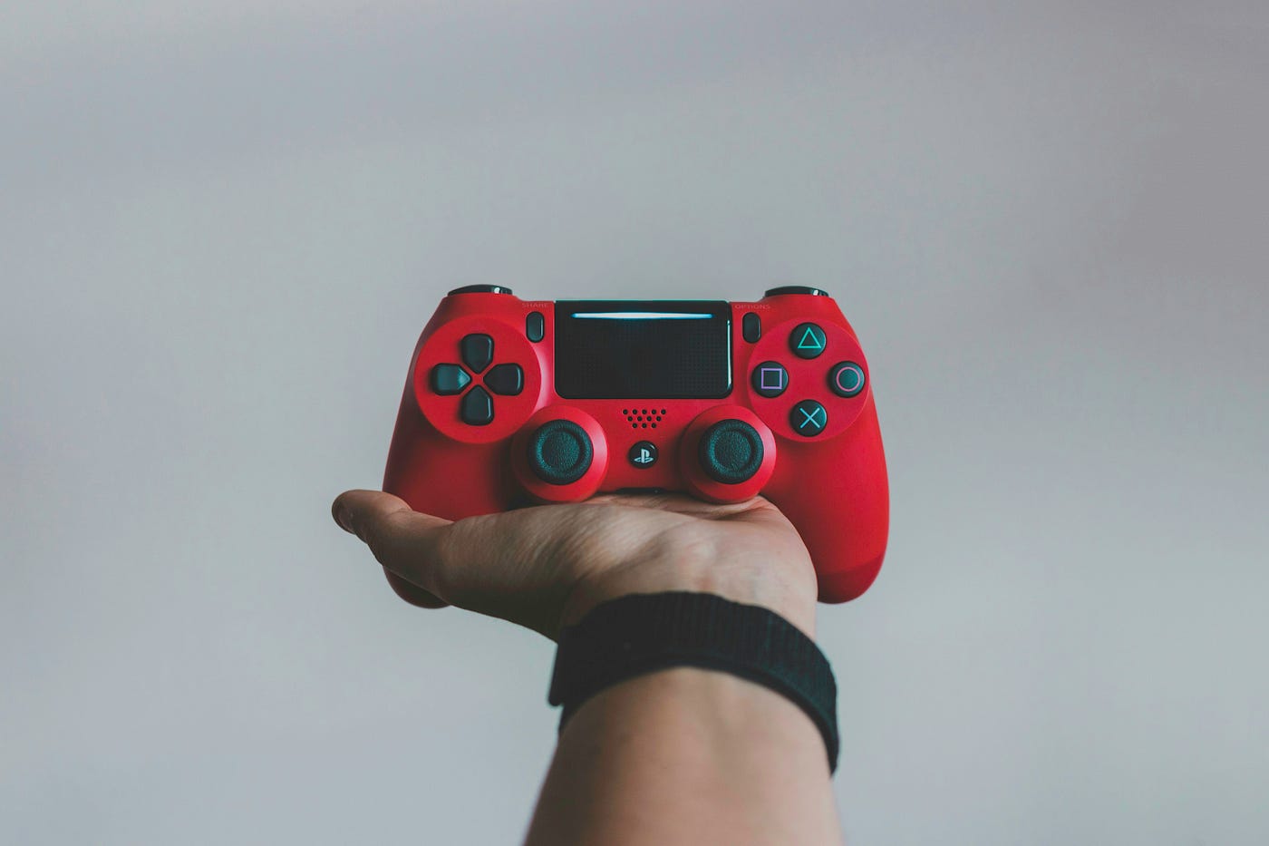 An outstretched palm holding a red games controller against a plain grey background.