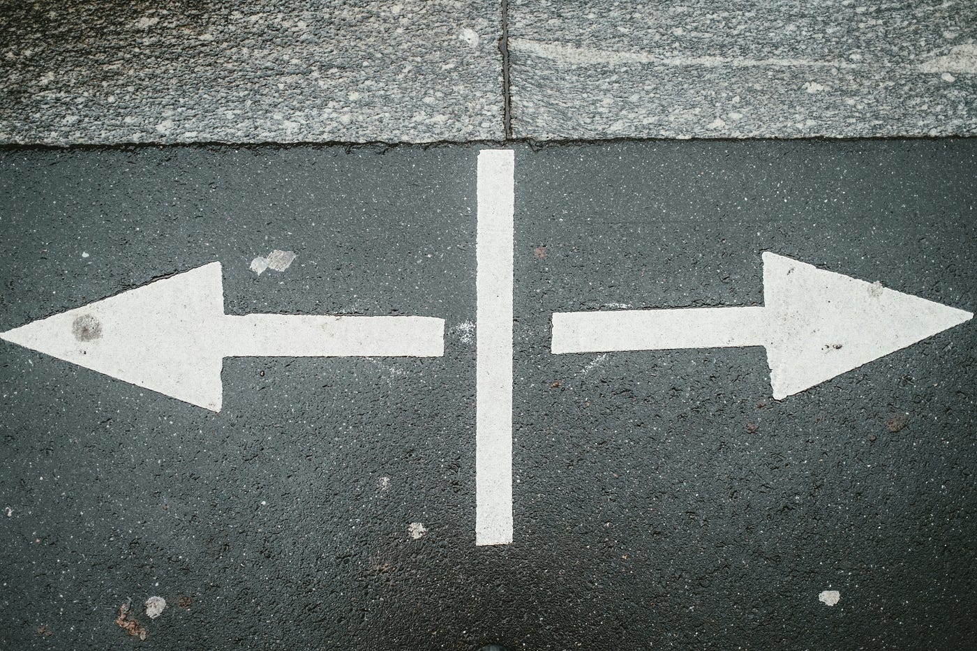 Two white arrows painted on asphalt pointing in opposite directions, separated by a single painted dividing line.