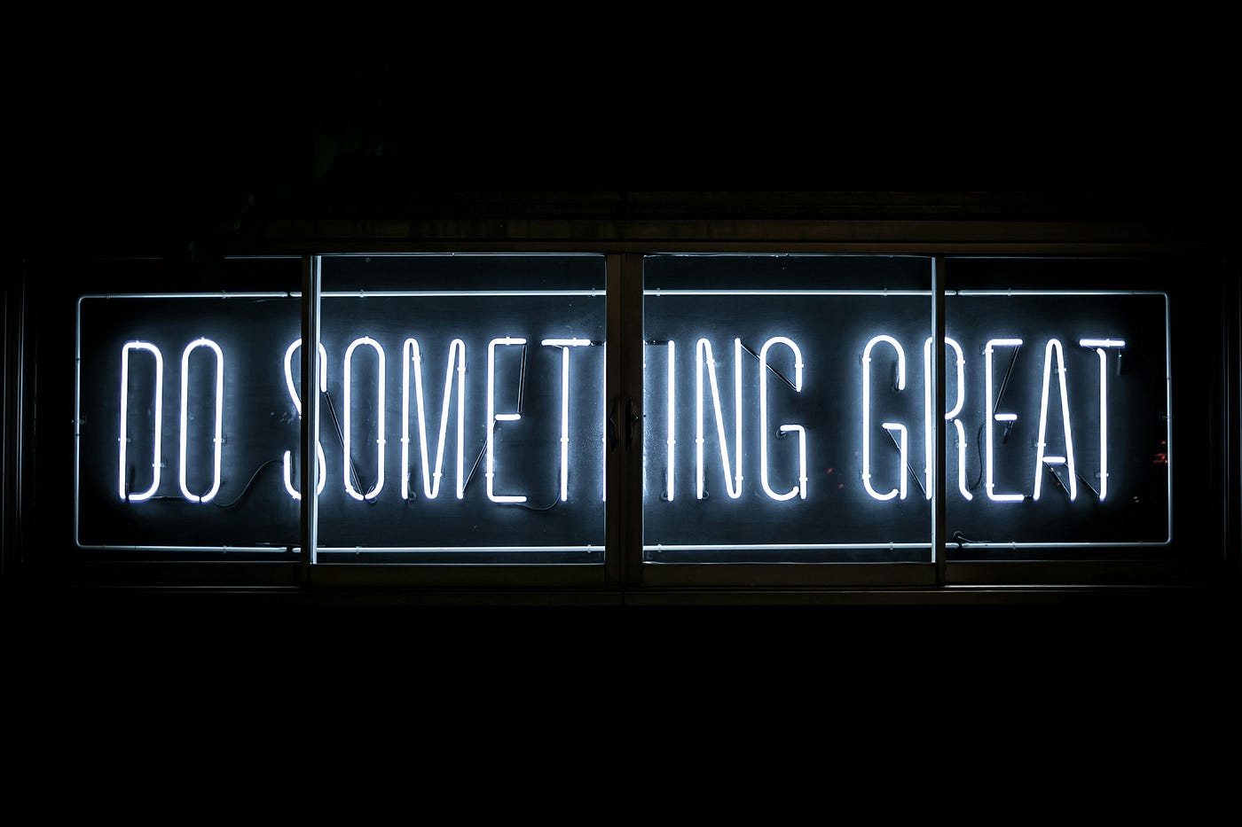 A white neon sign in a dark window reading 'DO SOMETHING GREAT'.